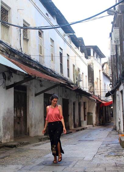 A woman walking down a narrow street lined with old buildings, some with visible wear and tear. 2