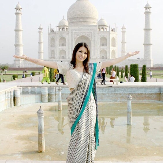 A person in a patterned saree with arms outstretched in front of the Taj Mahal. 1