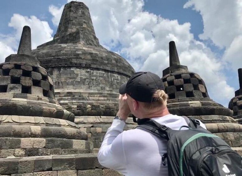 A person taking a photo of a large stone structure with a pointed top and smaller structures on either side. 1