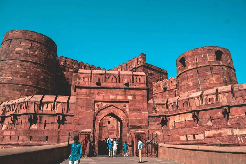 A historic fort with red sandstone walls, a large arched entrance, and two prominent round towers. 4