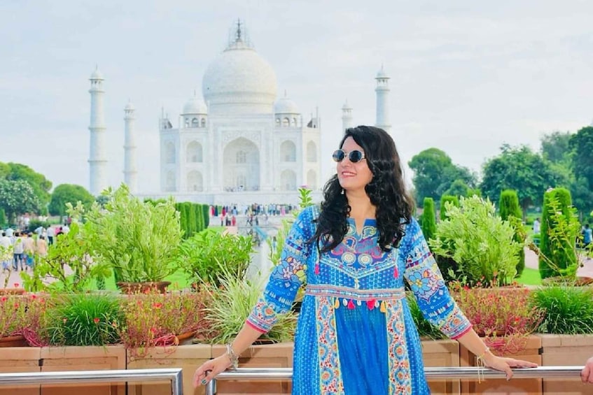 A person standing in front of the Taj Mahal with a garden and visitors in the background. 2