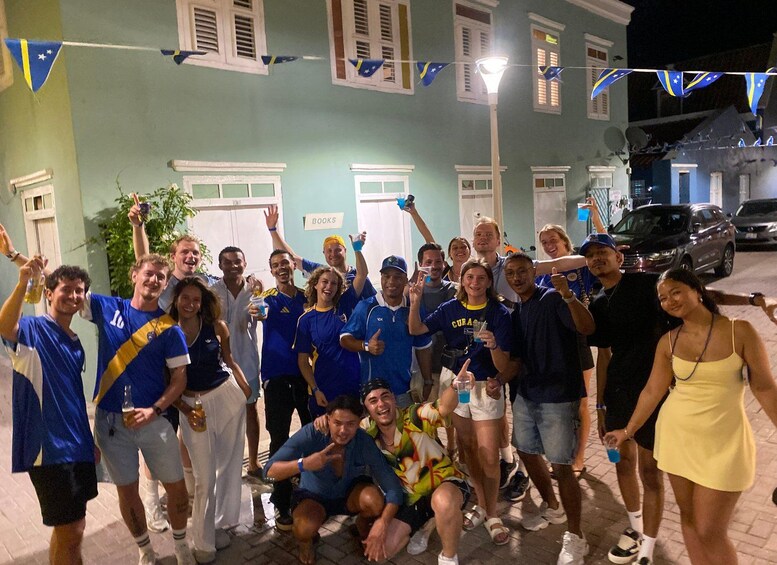 A group of people in blue and yellow sports jerseys posing for a photo in front of a building with a 'BOOKS' sign. 3