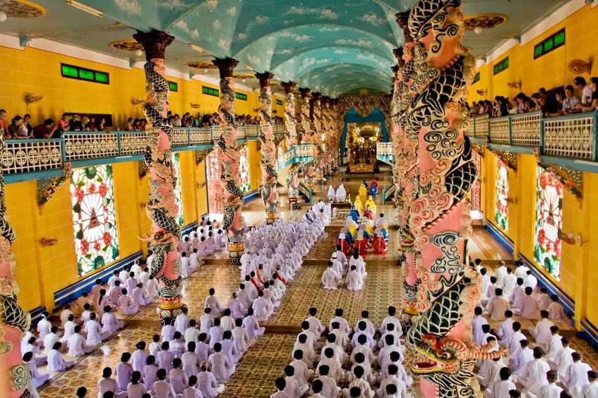 A temple interior with rows of people in white robes, ornate pillars, and a large dragon statue. 4