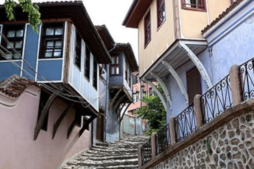 A narrow street with buildings on either side, a stone wall with a metal railing, and a staircase leading up. 2