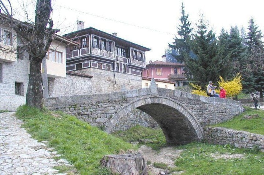A stone bridge over a stream, surrounded by stone walls and houses with traditional architecture. 1