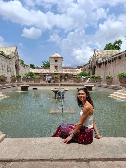 A woman sitting by a historic fountain with a building in the background. 1