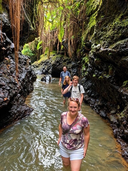 A group of people walking through a narrow, rocky stream surrounded by lush greenery. 5