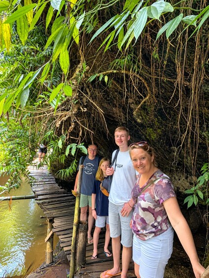 A group of people standing on a wooden bridge over a river, surrounded by dense greenery and trees. 4