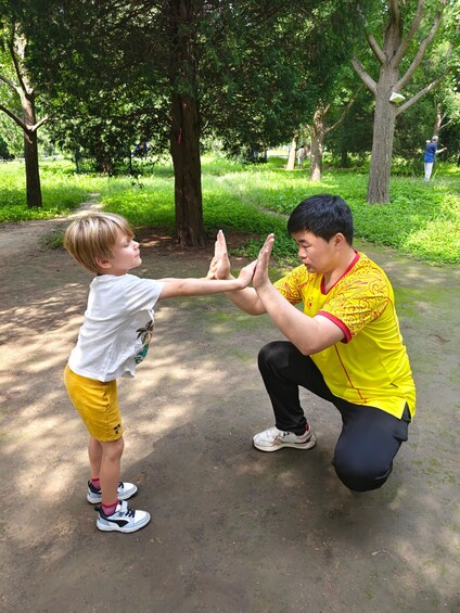 A person in a yellow shirt and black pants kneeling on the ground, interacting with a child in a white shirt and yellow shorts. 2