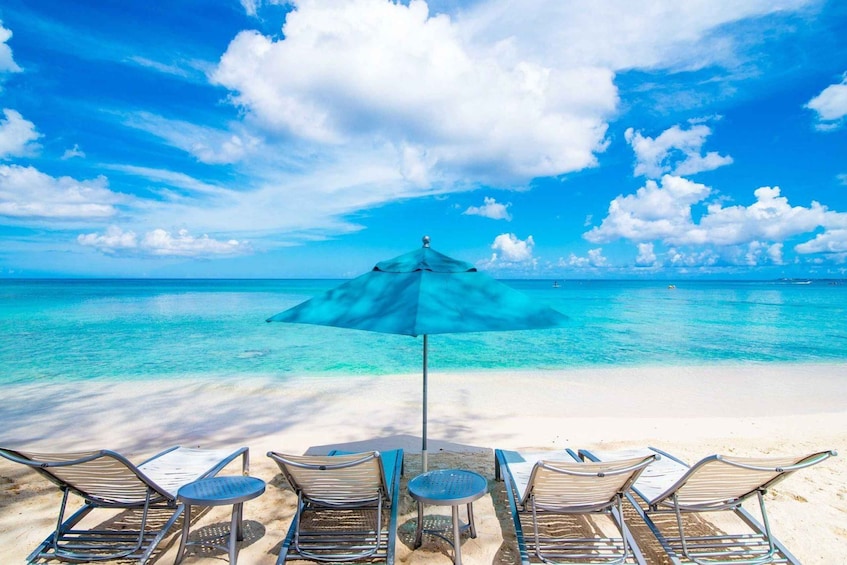 A beach with clear turquoise water, a blue umbrella, and lounge chairs. 2