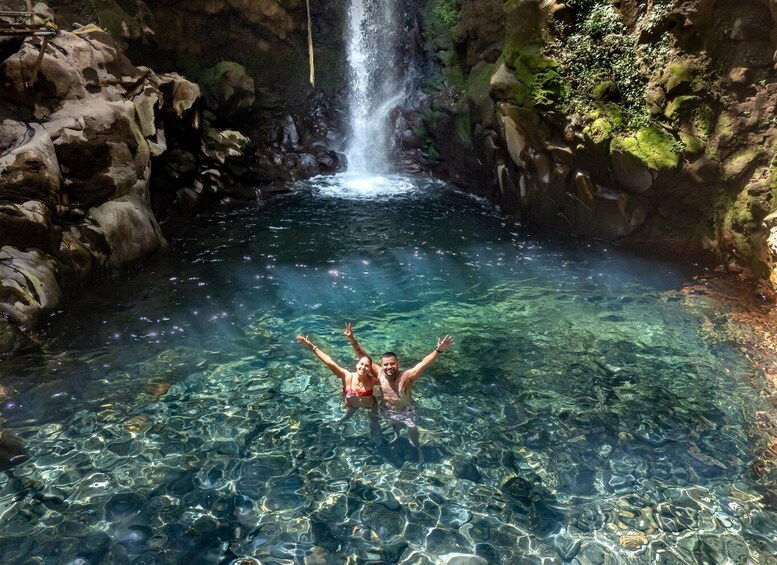 A person swimming in a clear pool with a waterfall in the background. 2