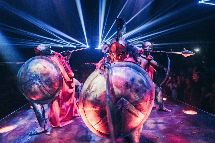 A stage with performers in metallic costumes and large shields. 2