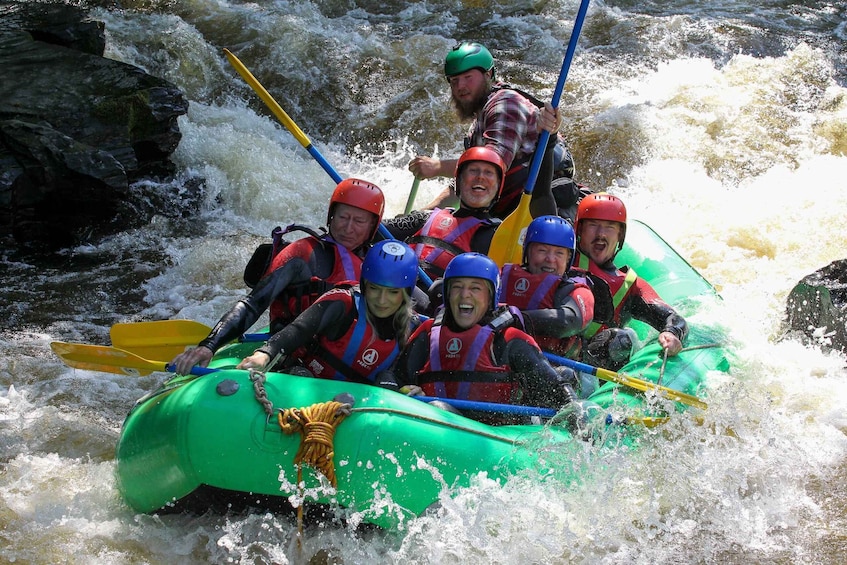 A group of people in a green raft navigating through a river with rapids. 3