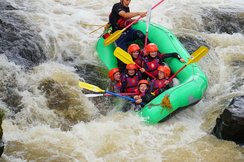 A group of people in a green raft navigating a turbulent river. 4