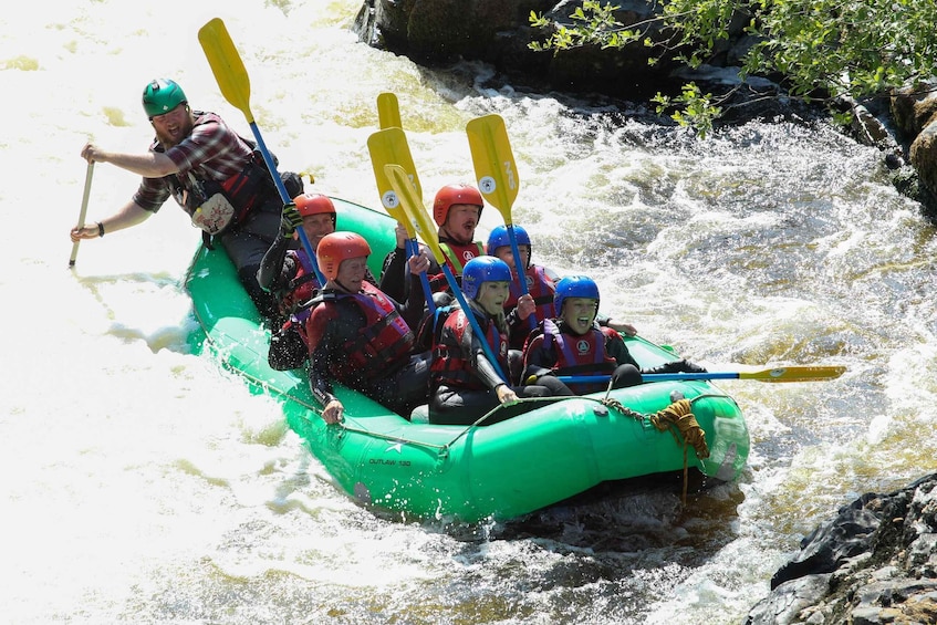 A group of people in a green inflatable raft navigating a fast-flowing river. 2