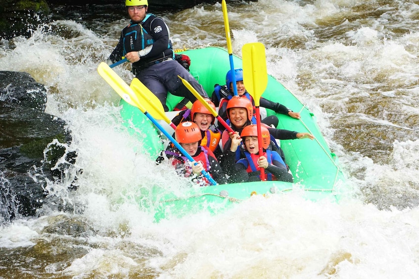 A group of people in a green raft navigating a river with rapids. 5
