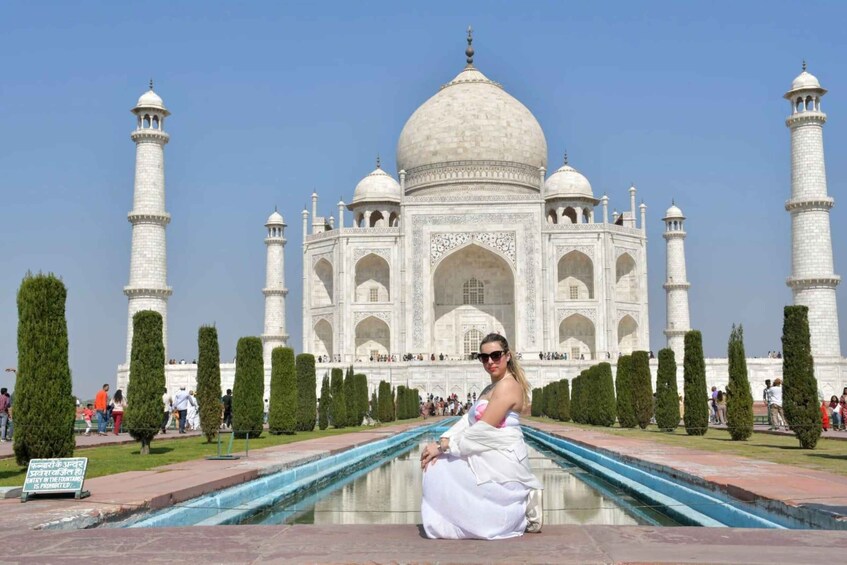 The Taj Mahal with a person in white dress sitting by the pool. 5