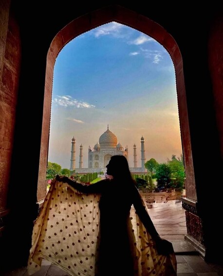 A silhouette of a person with a polka dot shawl, looking through an archway at the Taj Mahal. 4