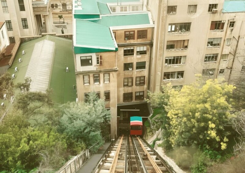 A train passing through a tunnel beneath a multi-story building with a green roof. 2