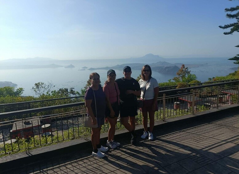 Four people standing on a paved walkway with a scenic view of a body of water and distant mountains. 5
