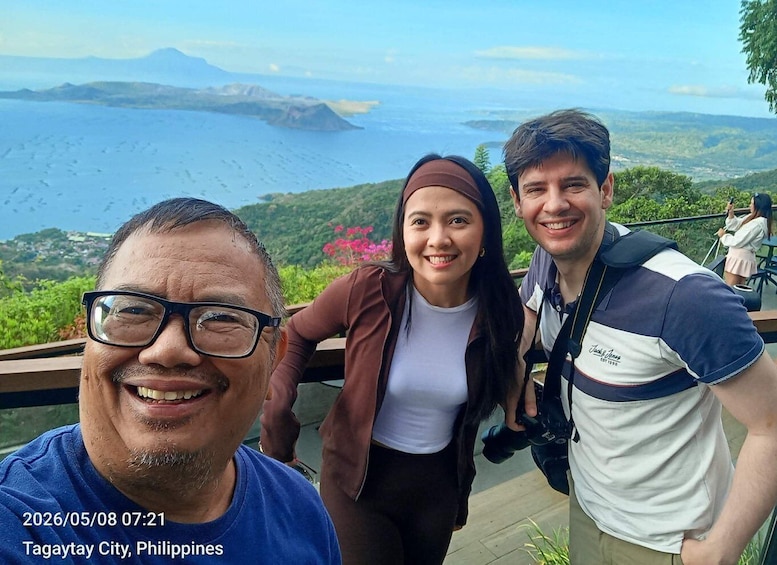 Three people on a deck overlooking a coastal landscape with mountains and a body of water. 5