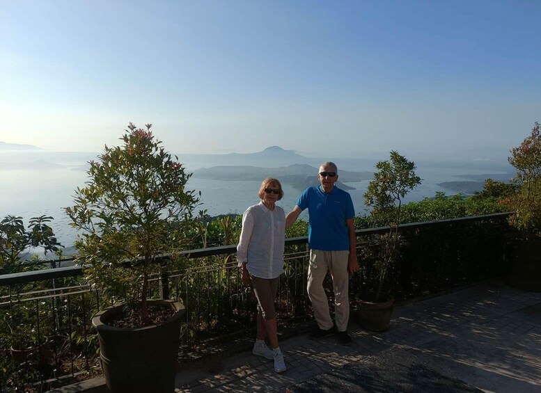 Two people standing on a terrace with a view of a body of water and mountains in the distance. 4