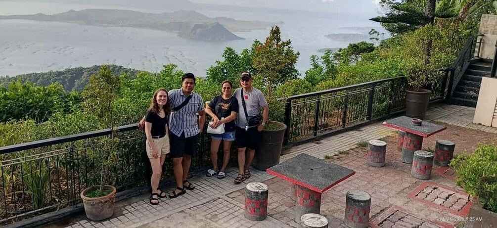A group of people standing on a terrace with a scenic view of a coastline and hills. 2