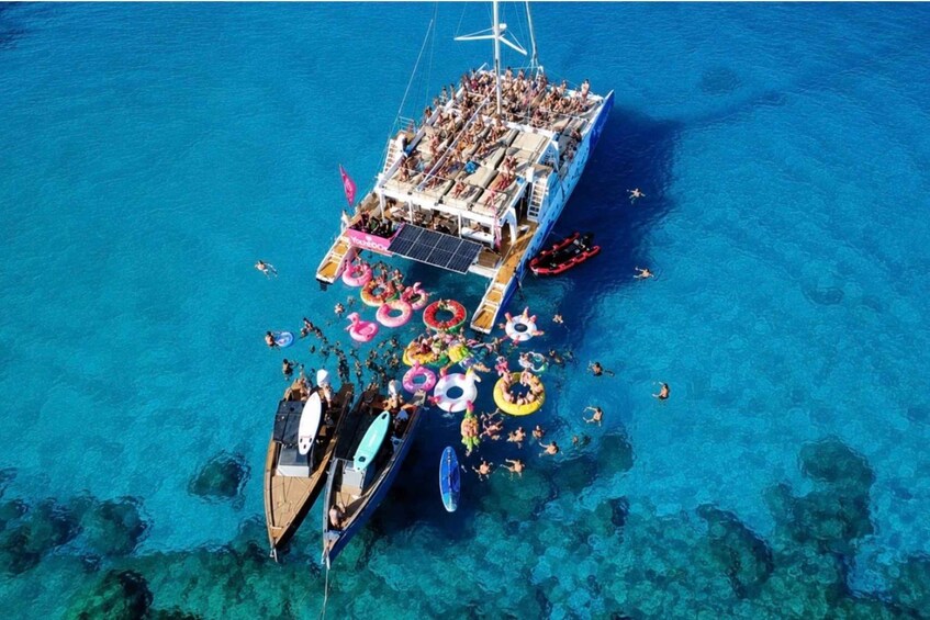 A large boat filled with people, surrounded by clear blue water and colorful inflatable rings. 4
