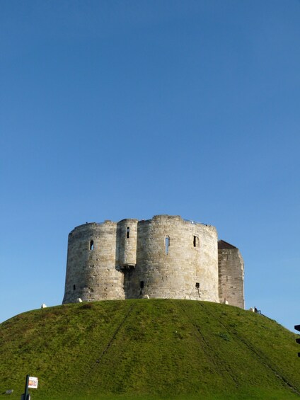 A historic stone castle on a grassy hill under a clear blue sky. 4
