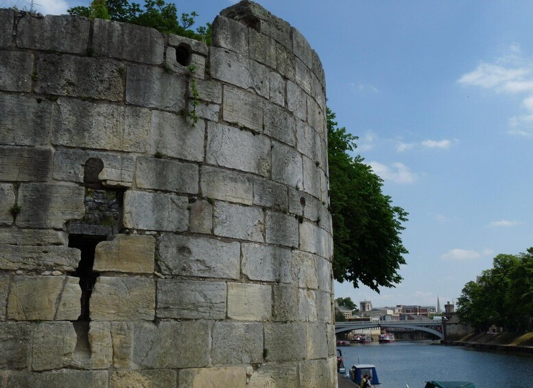 A stone wall with a large hole and a smaller hole, a river, and a bridge in the background. 3