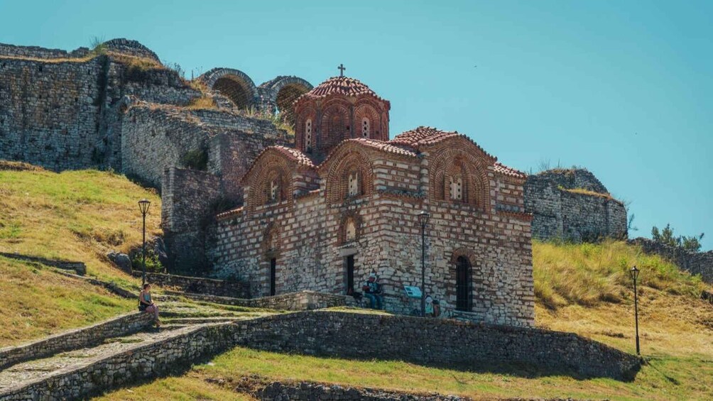 Una chiesa in pietra con una croce sulla sommità, circondata da rovine e dolci colline erbose. 5