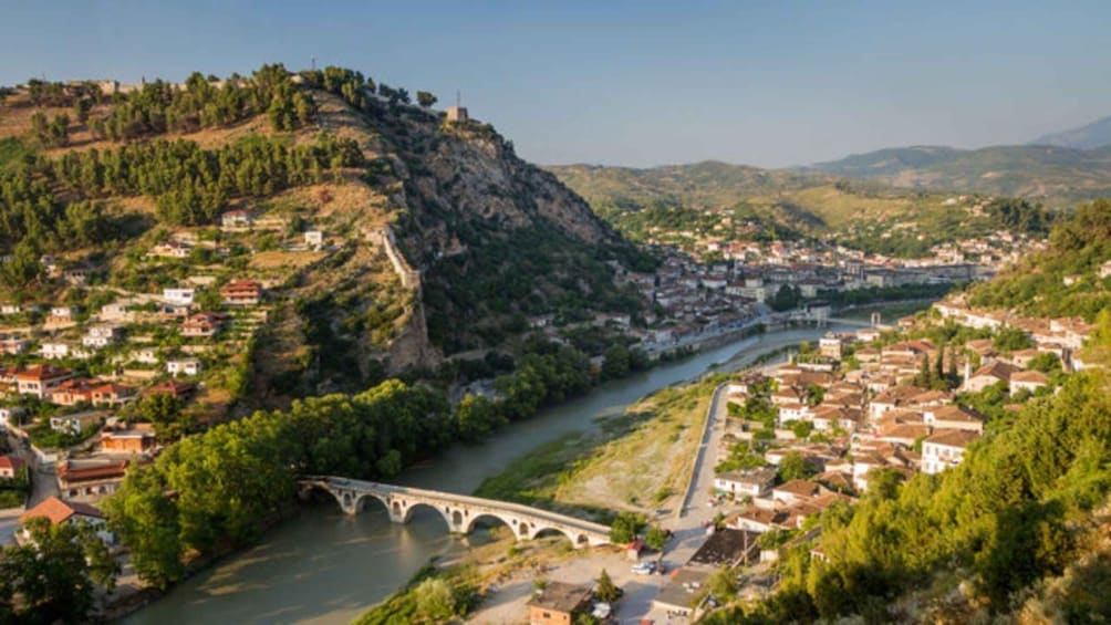 Un fiume che scorre attraverso una cittadina con un ponte, circondata da colline e vegetazione. 3