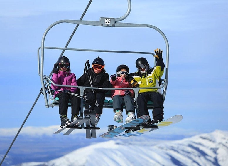 Four people on a ski lift with snow-covered mountains in the background. 3