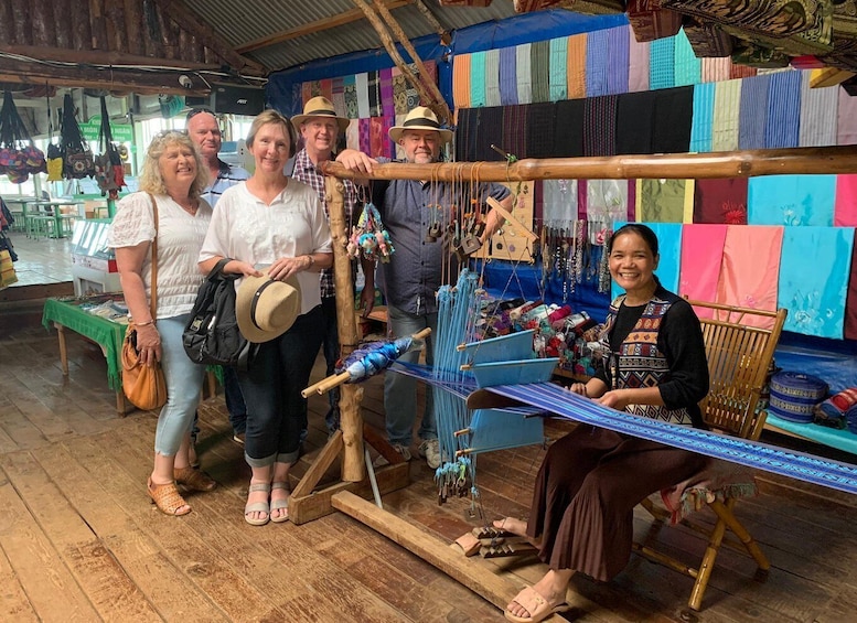 A group of people at a market stall with colorful textiles and a weaving loom. 3