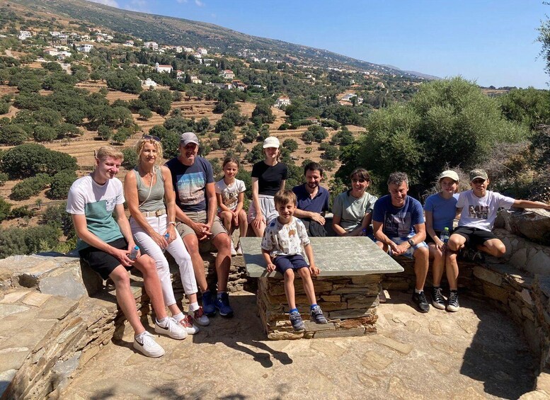 A group of people sitting on a stone bench overlooking a hilly landscape with scattered houses. 5