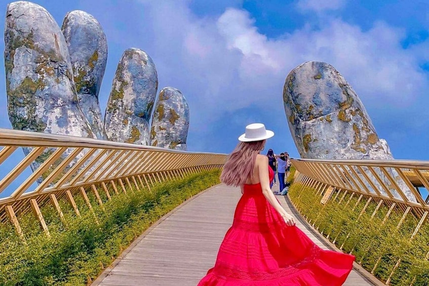 A woman in a red dress and white hat walking on a wooden boardwalk with large rock formations on either side. 1