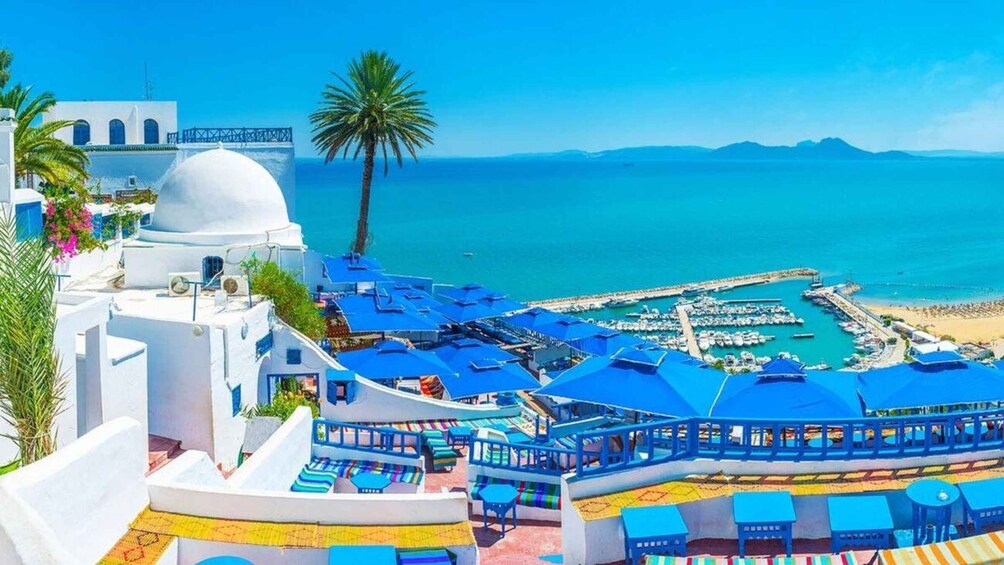 A coastal resort with white buildings, blue umbrellas, and a marina. 1