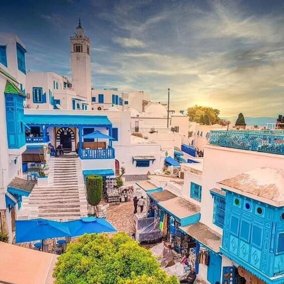 A coastal town with white and blue buildings, a prominent tower, and a staircase leading to a covered area. 3