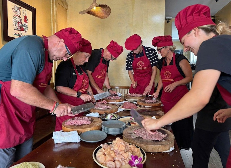 A group of people in red aprons and chef hats preparing food at a wooden table. 5