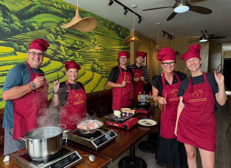 A group of people in red aprons cooking with a stove, pots, and a grill. 4