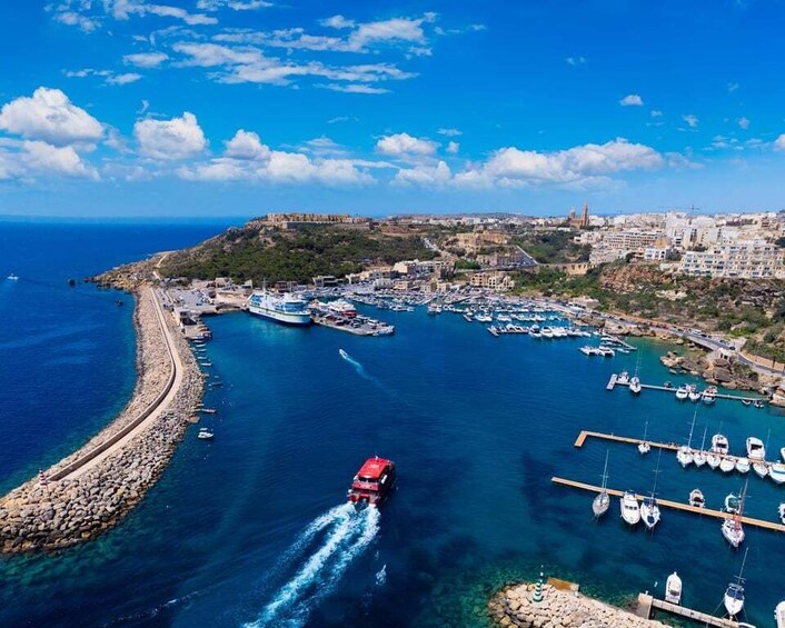 A coastal town with a marina, boats, and a red boat moving through the water. 3