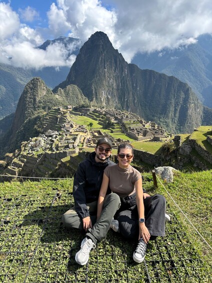 A couple sitting on a grassy area with Machu Picchu in the background. 2