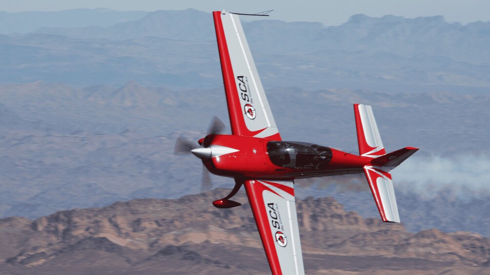 A red and white airplane with "SCA" on its wings flying over a mountainous landscape. 2