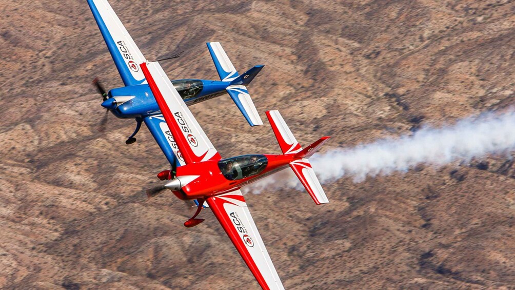 Two small aircraft flying in formation with smoke trailing from the red plane. 5