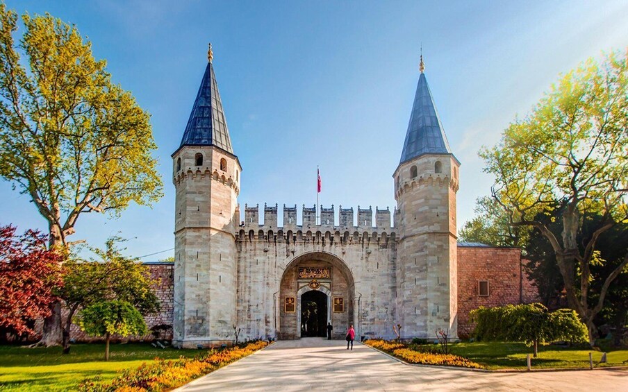 A historic stone gate with two towers, surrounded by trees and a clear sky. 1
