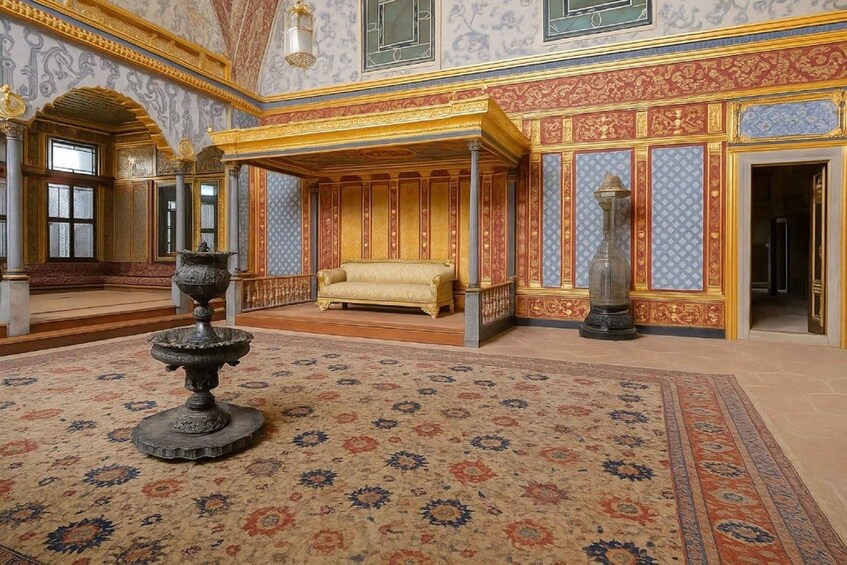 An ornate room with a canopy bed, a large vase, and intricate wall designs. 2
