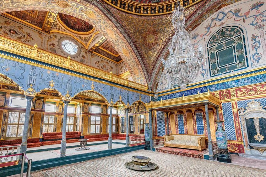 An ornate interior with intricate blue and gold patterns, a chandelier, and a large vase. 3