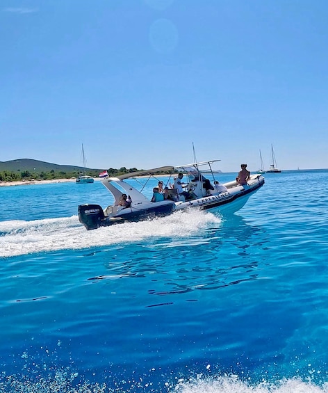A blue boat with 'EXPERIENCE' written on the side, moving through clear blue water with a sandy beach and sailboats in the background. 5
