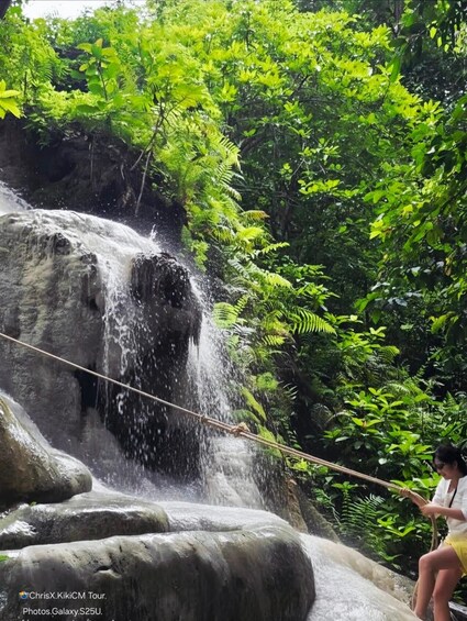 A waterfall in a lush forest with a person sitting on a rock nearby. 4
