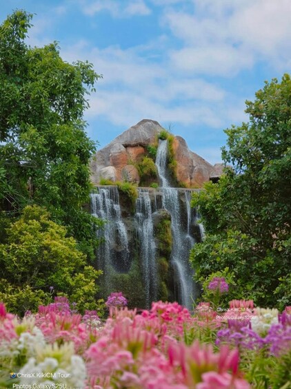 A waterfall cascading over a rock formation surrounded by lush greenery and colorful flowers. 3